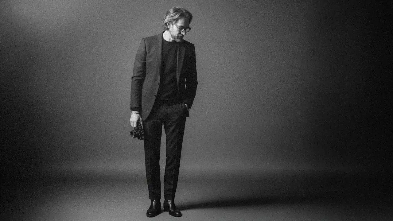 Un uomo con un completo elegante tiene una macchina fotografica, un autoritratto creativo che cattura l'essenza dell'artista.