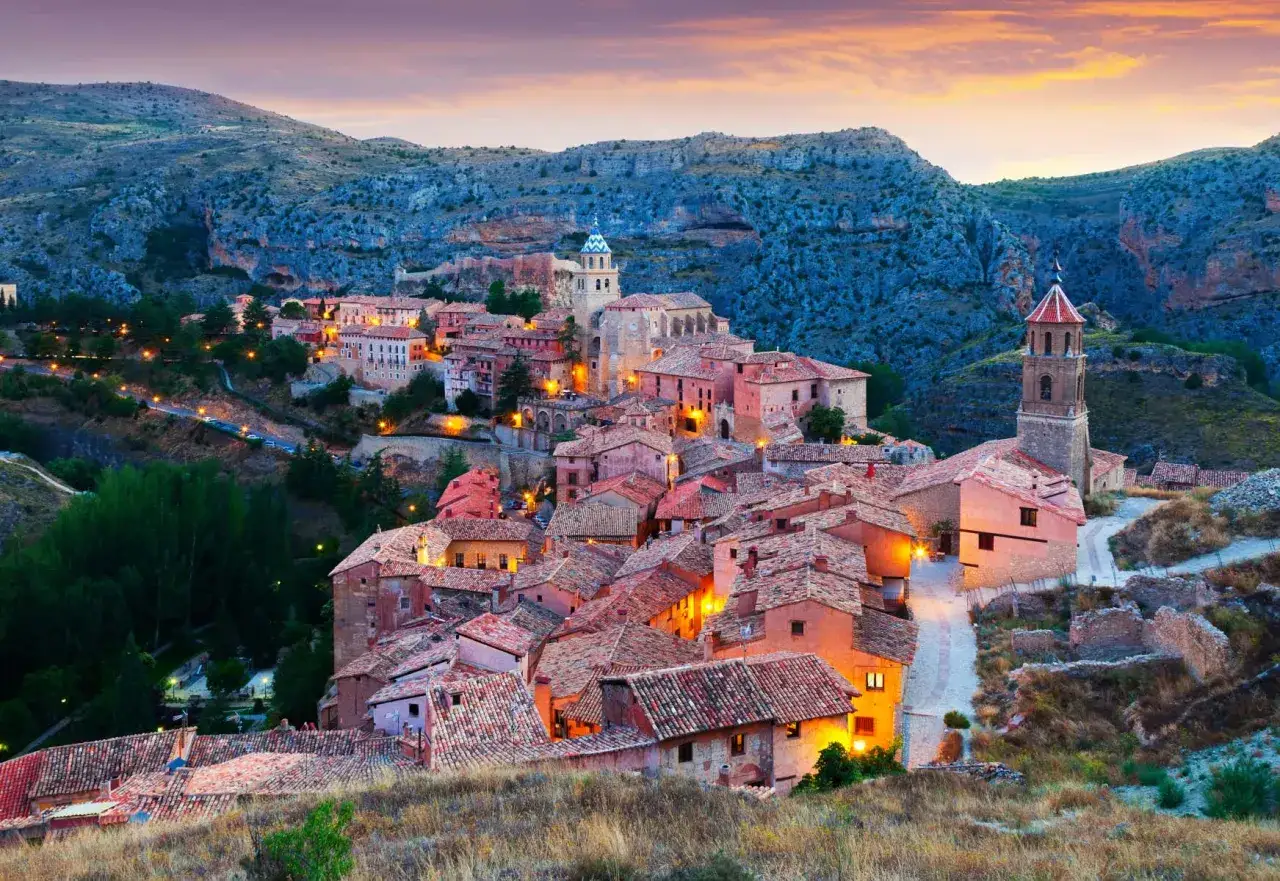 Pueblo medieval iluminado al atardecer, con tejados rojos y torres, uno de los pueblos más bonitos de Teruel.