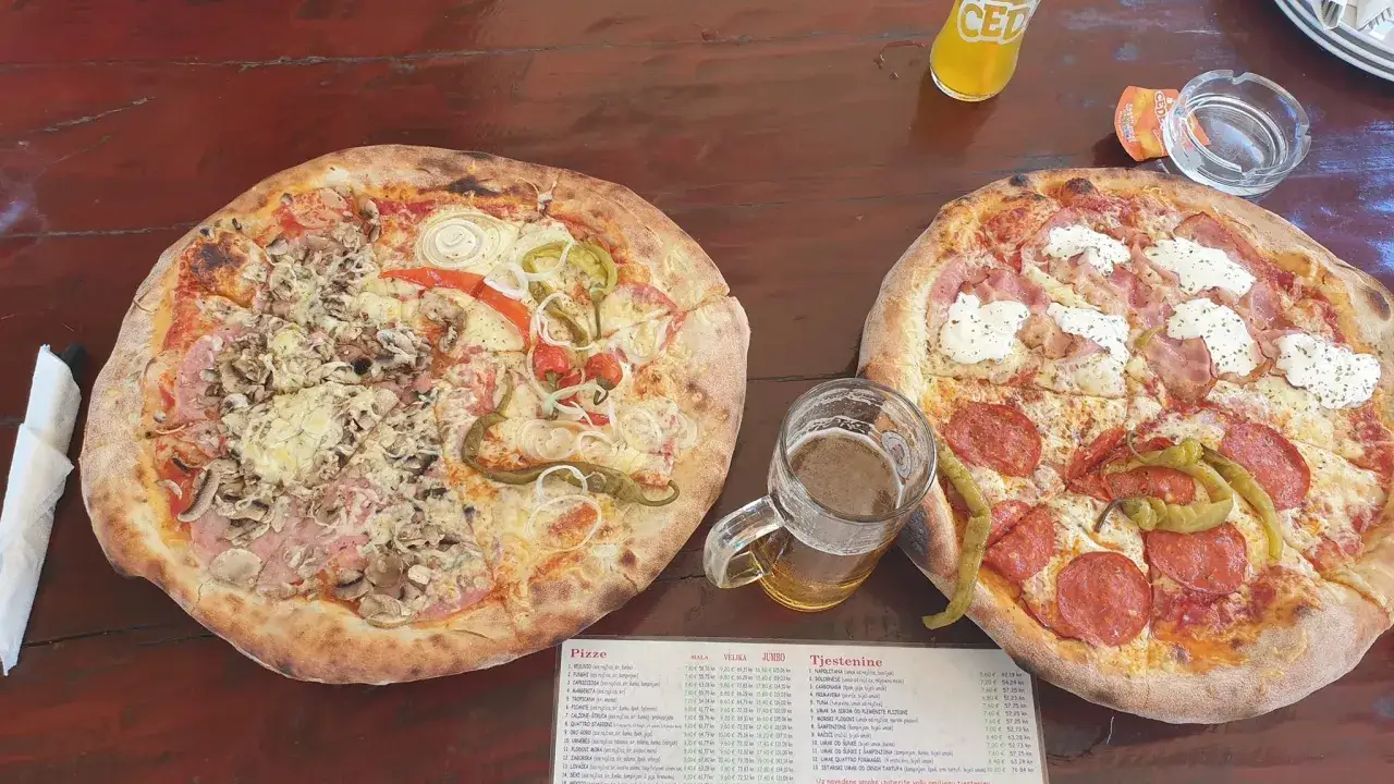 Dwie pizze i piwo na drewnianym stole. Ceny pizzy w Chorwacji są widoczne na menu.