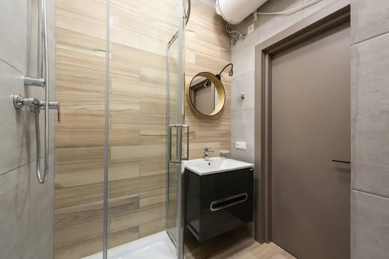 Moderno ba&ntilde;o con ducha de cristal, lavabo suspendido y espejo redondo. Ideal para calcular el precio reforma ba&ntilde;o peque&ntilde;o.