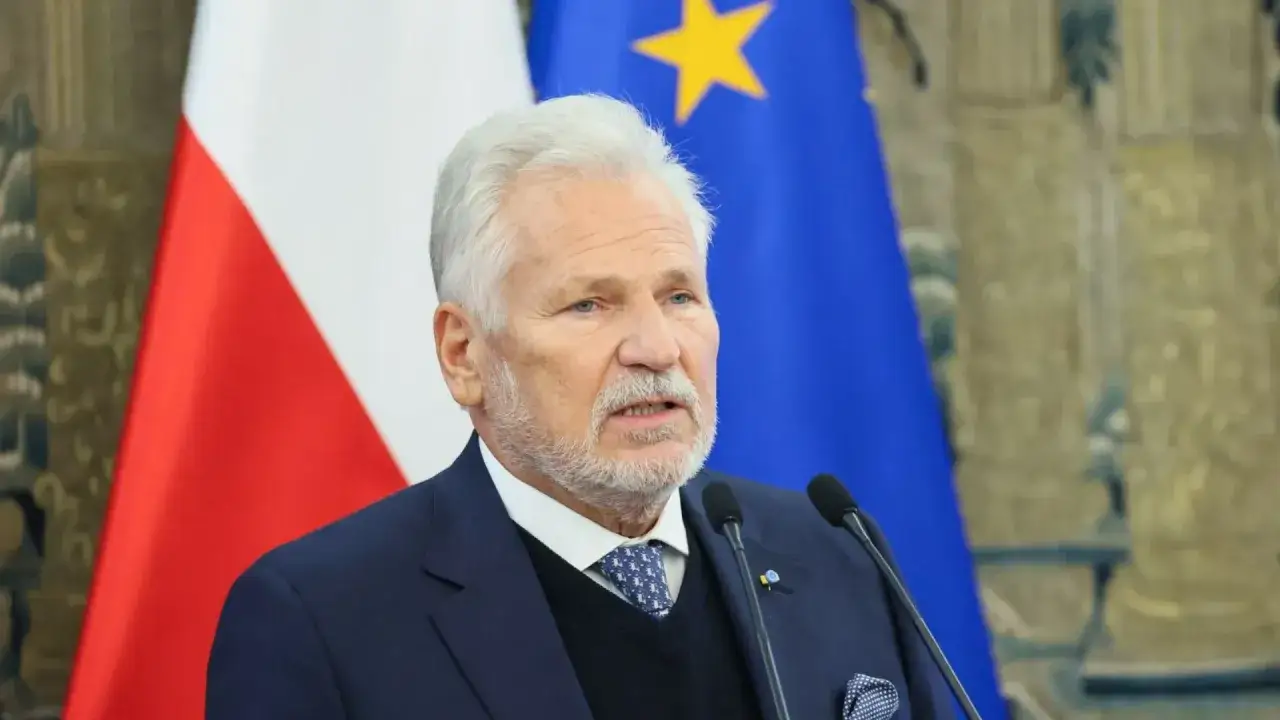 Aleksander Kwaśniewski, były prezydent, przemawia na tle flag Polski i UE. Jego prezydentura to ważny rozdział w historii Polski.