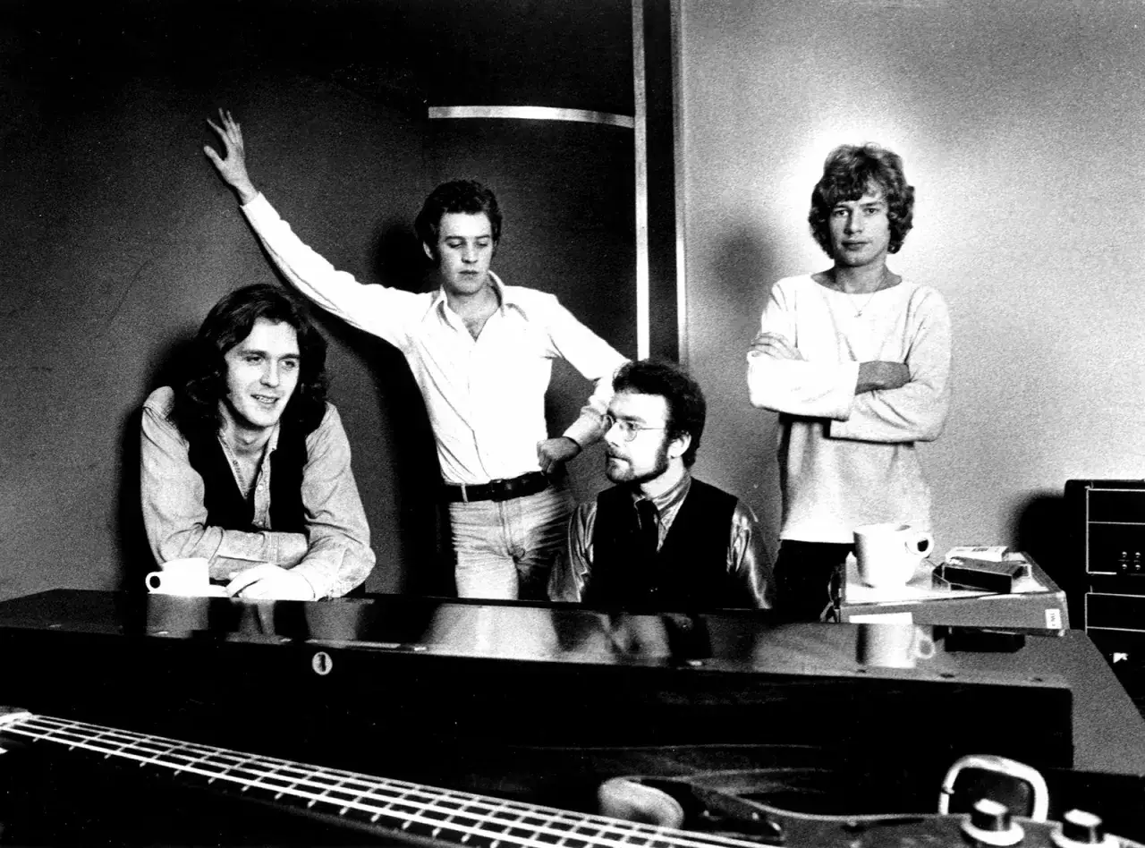 Les membres de King Crimson posent pour une photo. L'un d'eux est penché sur un piano, un autre a le bras levé.