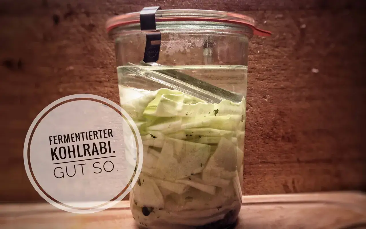 Ein Glas mit Kohlrabi, der fermentiert. Die Kohlrabistücke sind in Salzlake eingelegt und mit einem Gewicht beschwert.