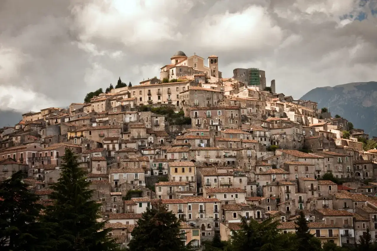 A densely packed hillside village, one of the many charming cities in Calabria, Italy, with terracotta roofs and a prominent church.