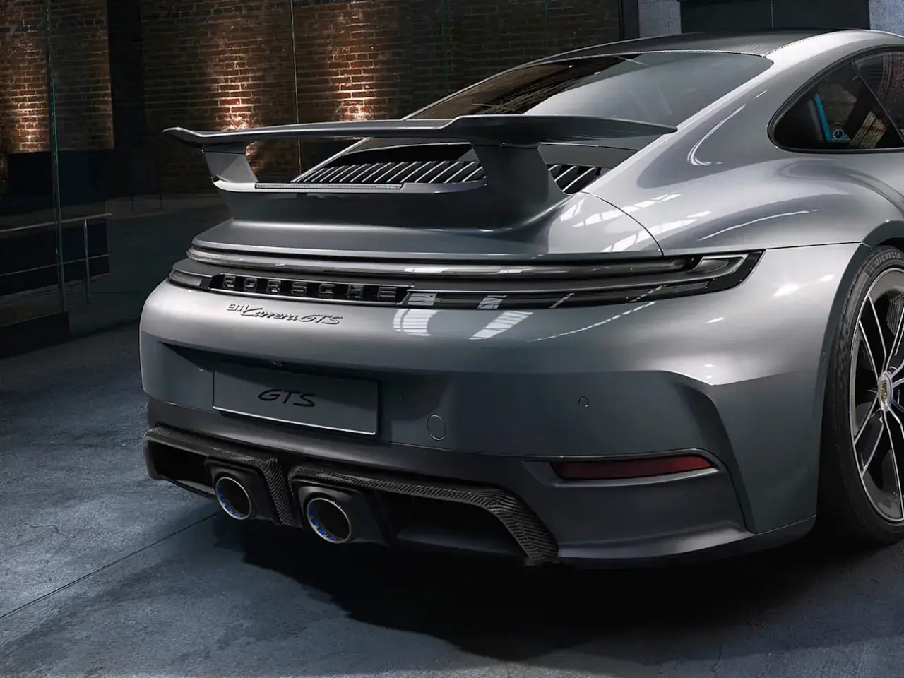Grauer Porsche 911 Carrera GTS von hinten mit markantem Heckspoiler und Carbon-Diffusor.