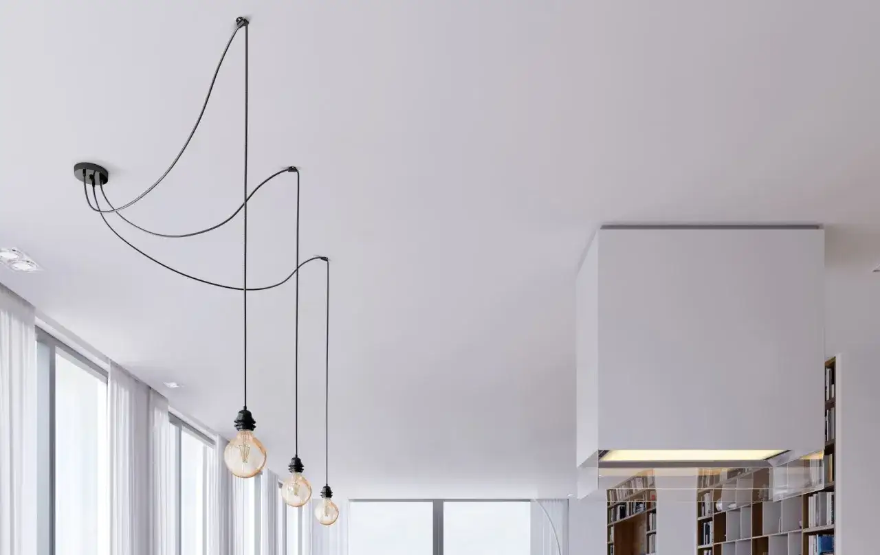 Une pose lampe moderne avec trois ampoules suspendues par des fils noirs, créant un éclairage d'ambiance dans un salon épuré.