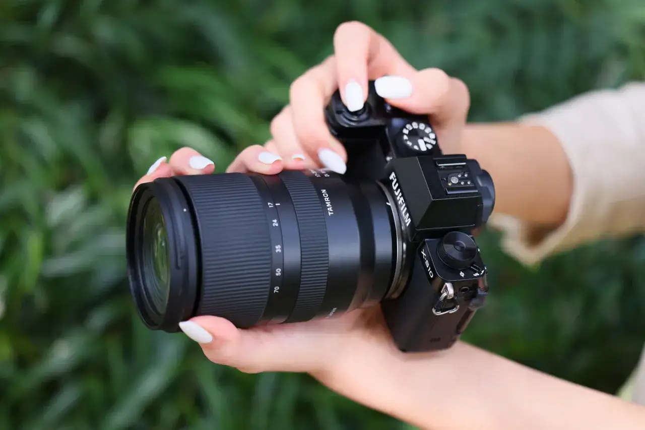 Dłonie z białym lakierem trzymają aparat Fujifilm z obiektywem Tamron 17-70 mm, gotowe do uchwycenia piękna natury.