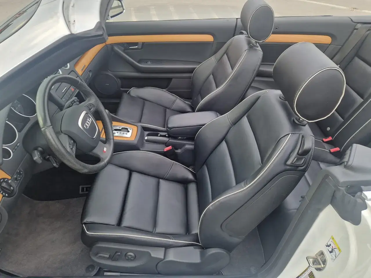 Wnętrze kabrioletu Audi B7 z czarną skórzaną tapicerką i drewnianymi wstawkami. Widok na fotele, deskę rozdzielczą i kierownicę.