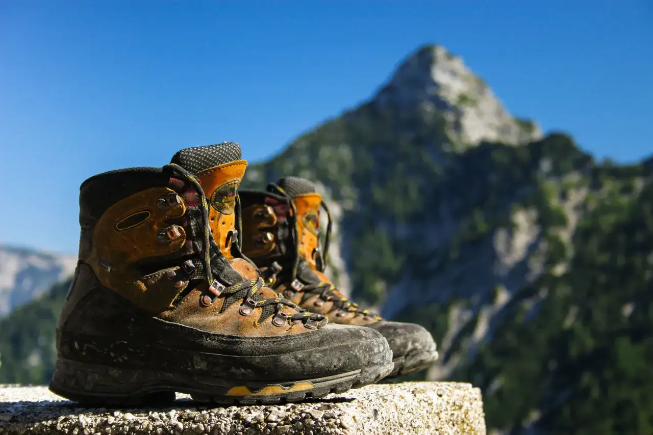 Well-worn hiking boots rest on a stone ledge, ready for adventure. Their sturdy design promises comfort and support, showcasing the benefits of hiking boots for any trail.
