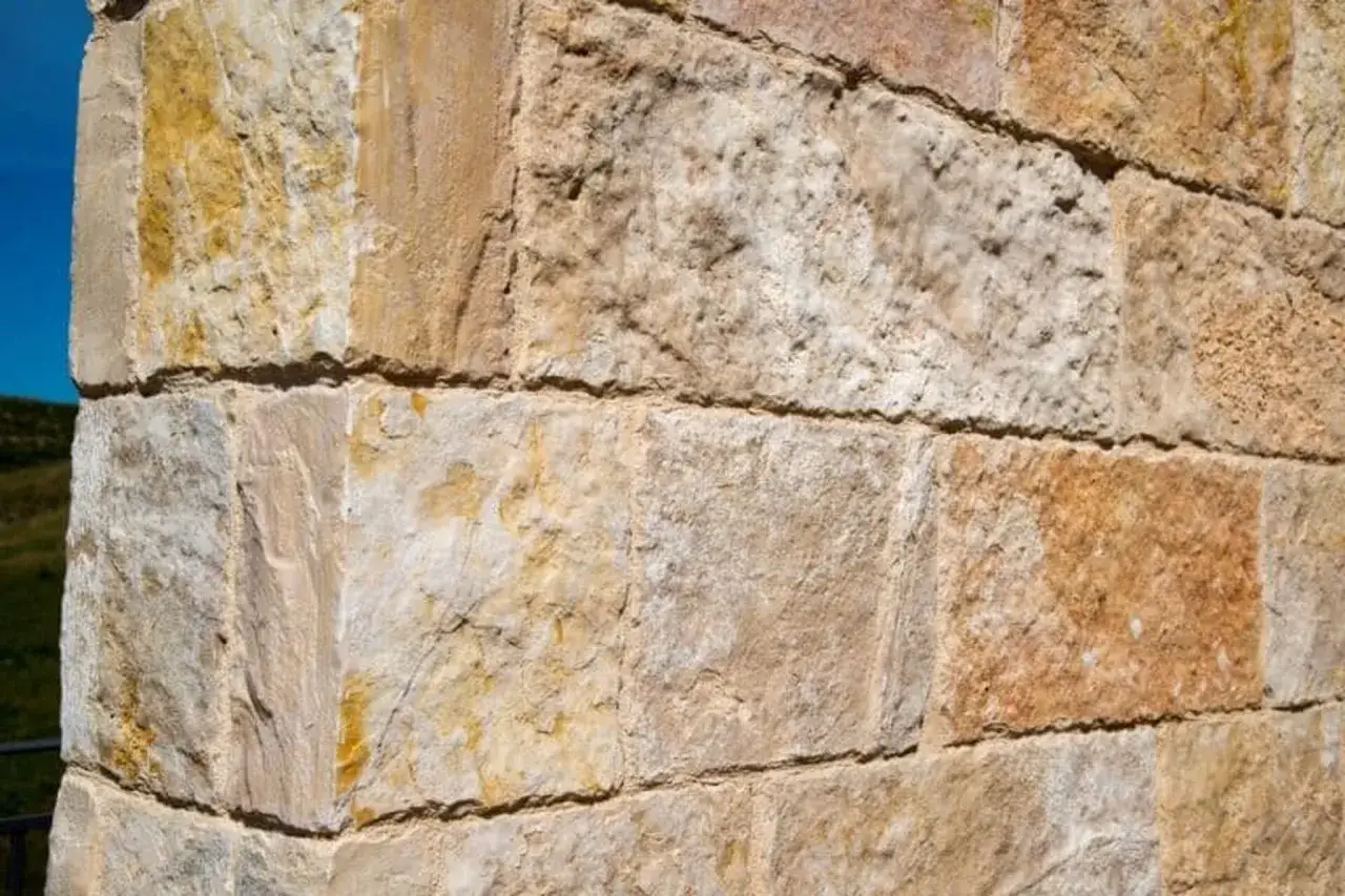 Gros plan sur un mur en pierre de construction, montrant divers types de pierres aux teintes beiges et ocres, avec des textures vari&eacute;es.