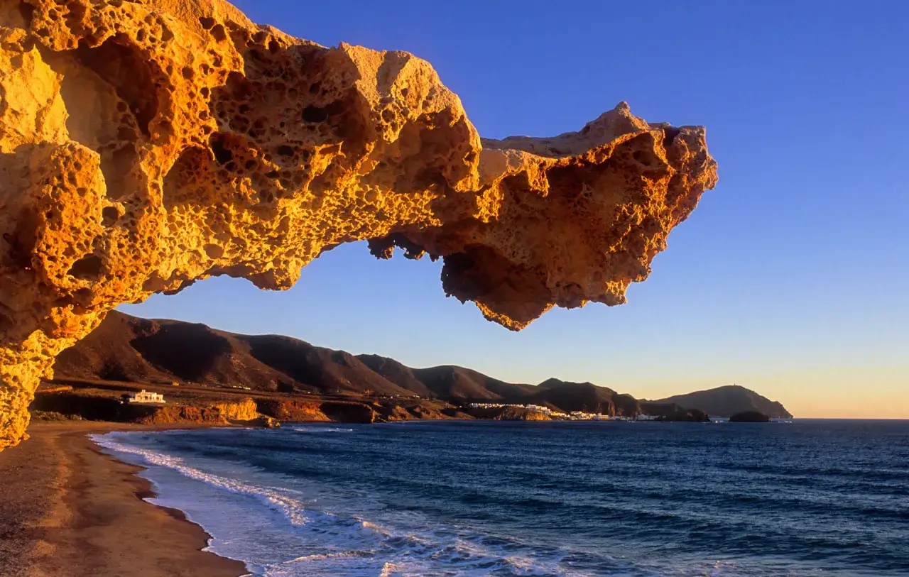 Roca erosionada ilumina la costa de Cabo de Gata, con el mar azul y montañas al fondo.