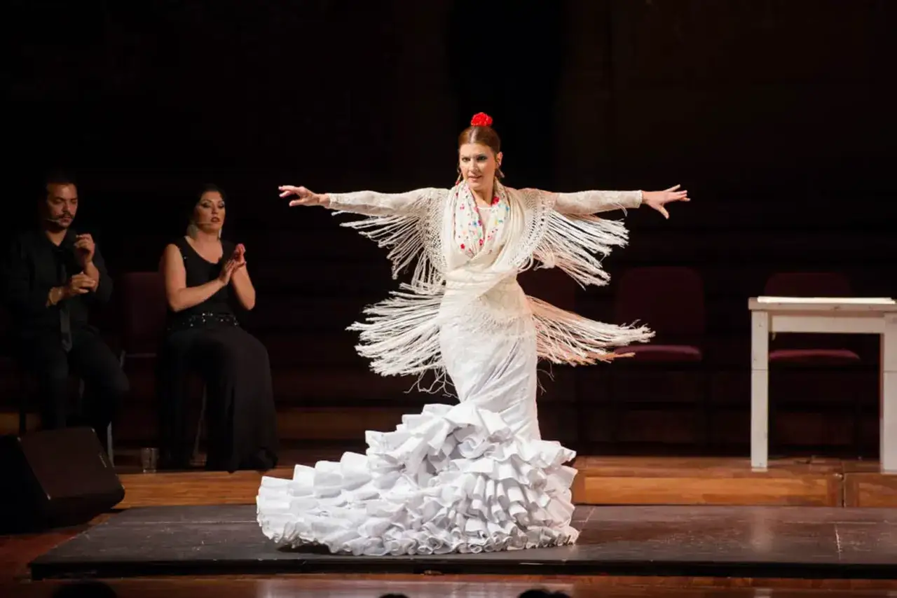 Bailaora de flamenco con vestido blanco y mantón de flecos, capturando el significado del flamenco en su expresión.