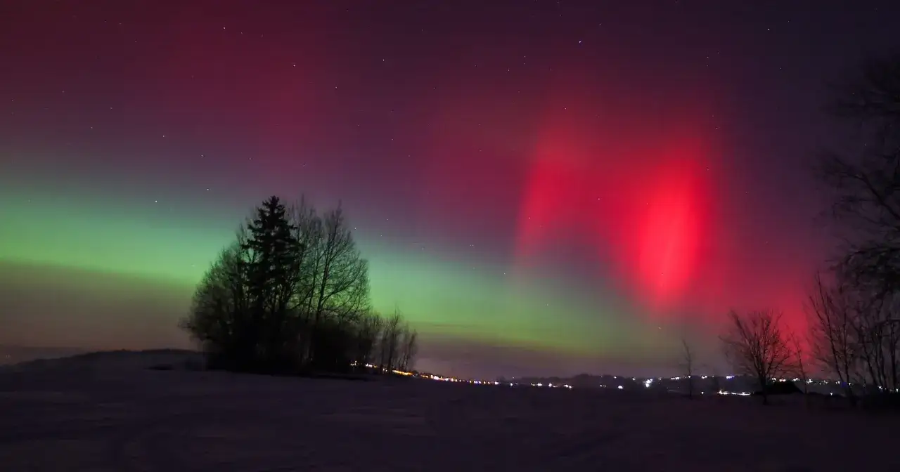 Nocne niebo rozświetlone zieloną i czerwoną zorzą polarną nad ośnieżonym krajobrazem.
