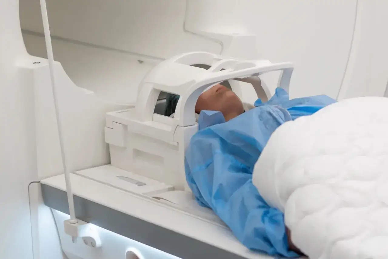 Pacjent leży w aparacie do rezonansu głowy, otoczony białym sprzętem medycznym.