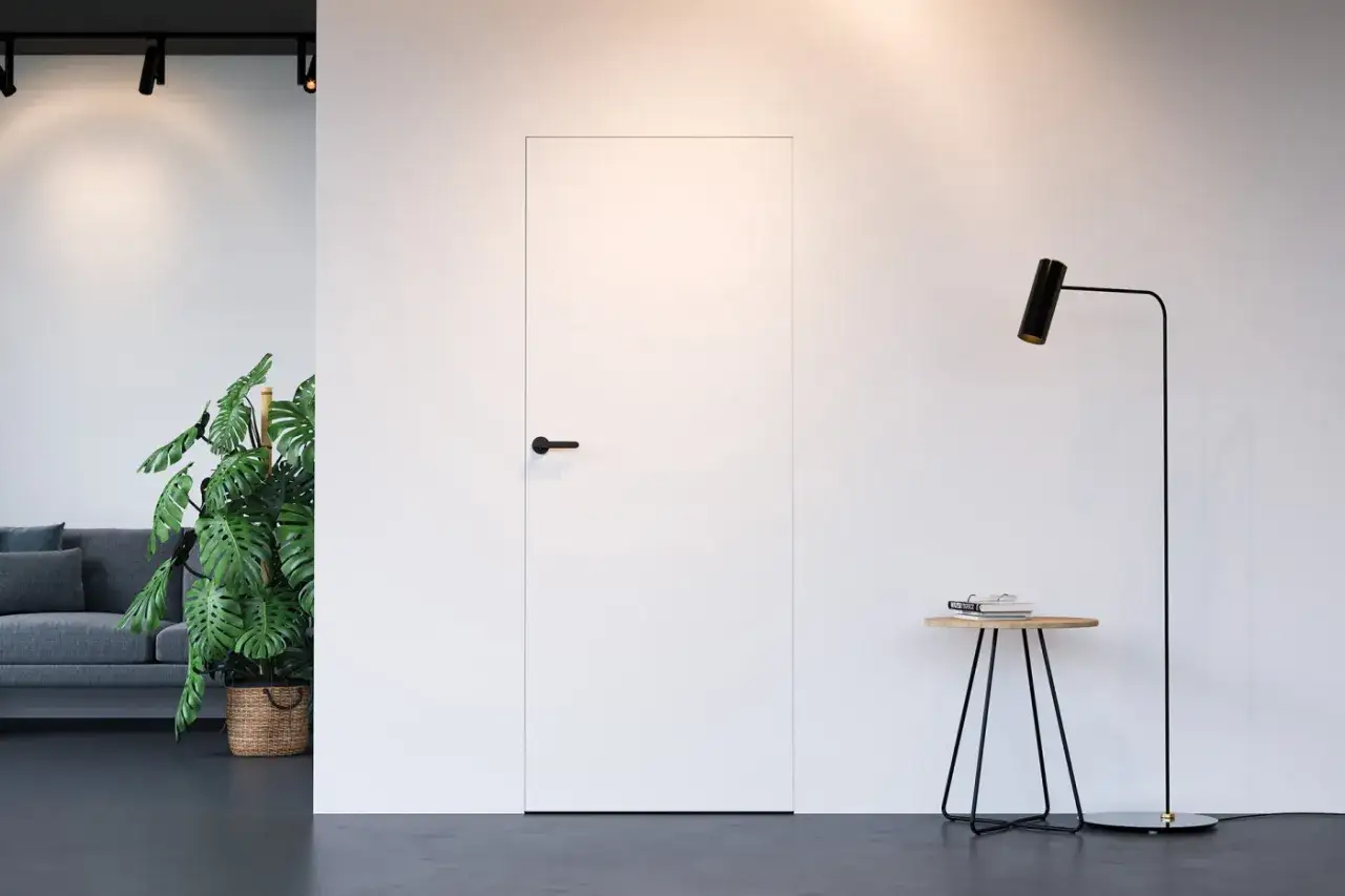 Minimalistyczne wnętrze z ukrytymi drzwiami, sofą, rośliną i lampą. Eleganckie drzwi ukryte w ścianie, tworzące spójne aranżacje.
