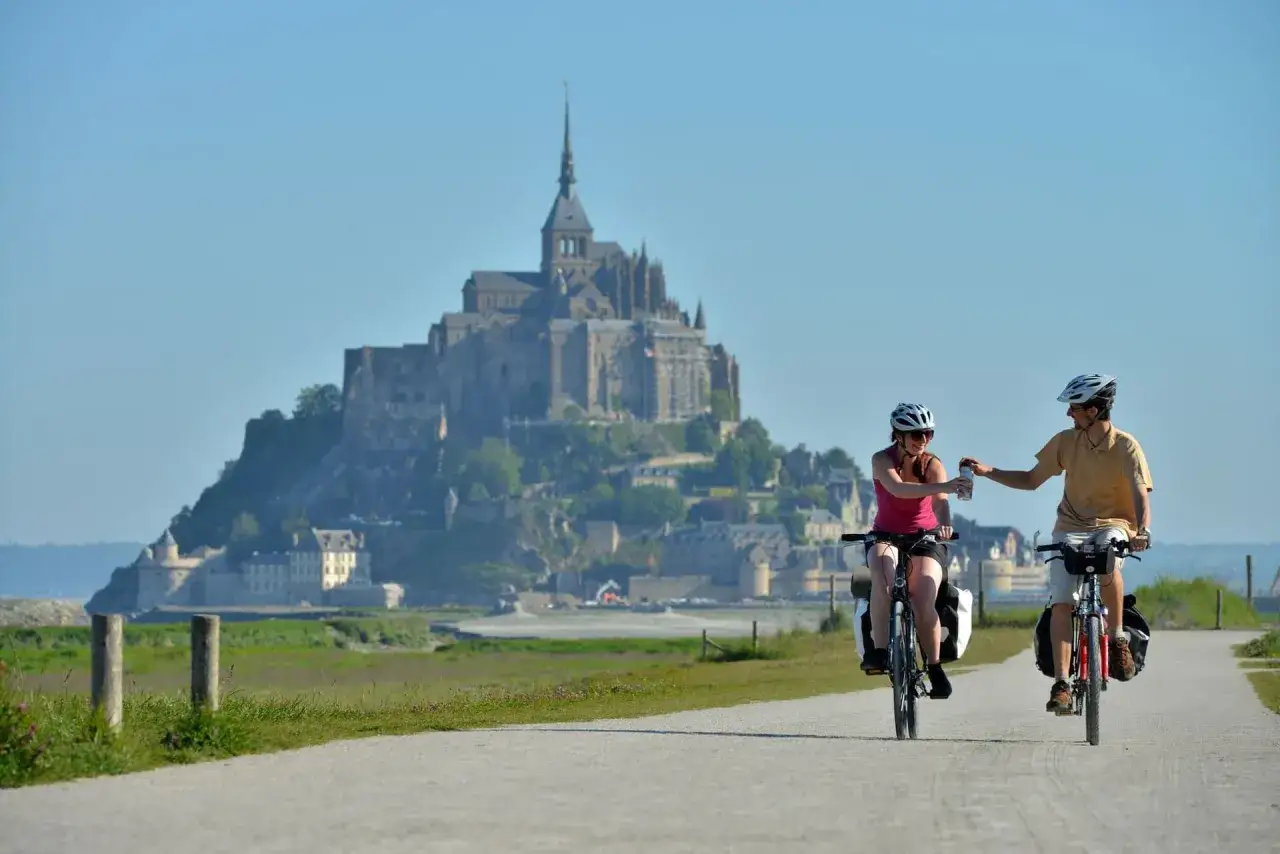 Couple on a scenic path enjoying Normandy bike tours, with Mont Saint-Michel in the background.