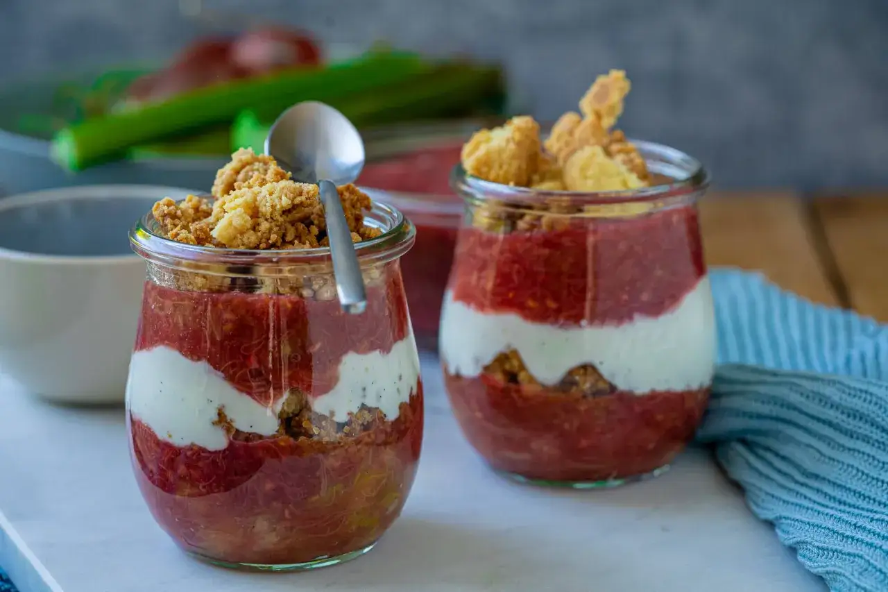 Zwei Gl&auml;ser mit geschichtetem Rhabarber-Dessert, garniert mit knusprigem Crumble.