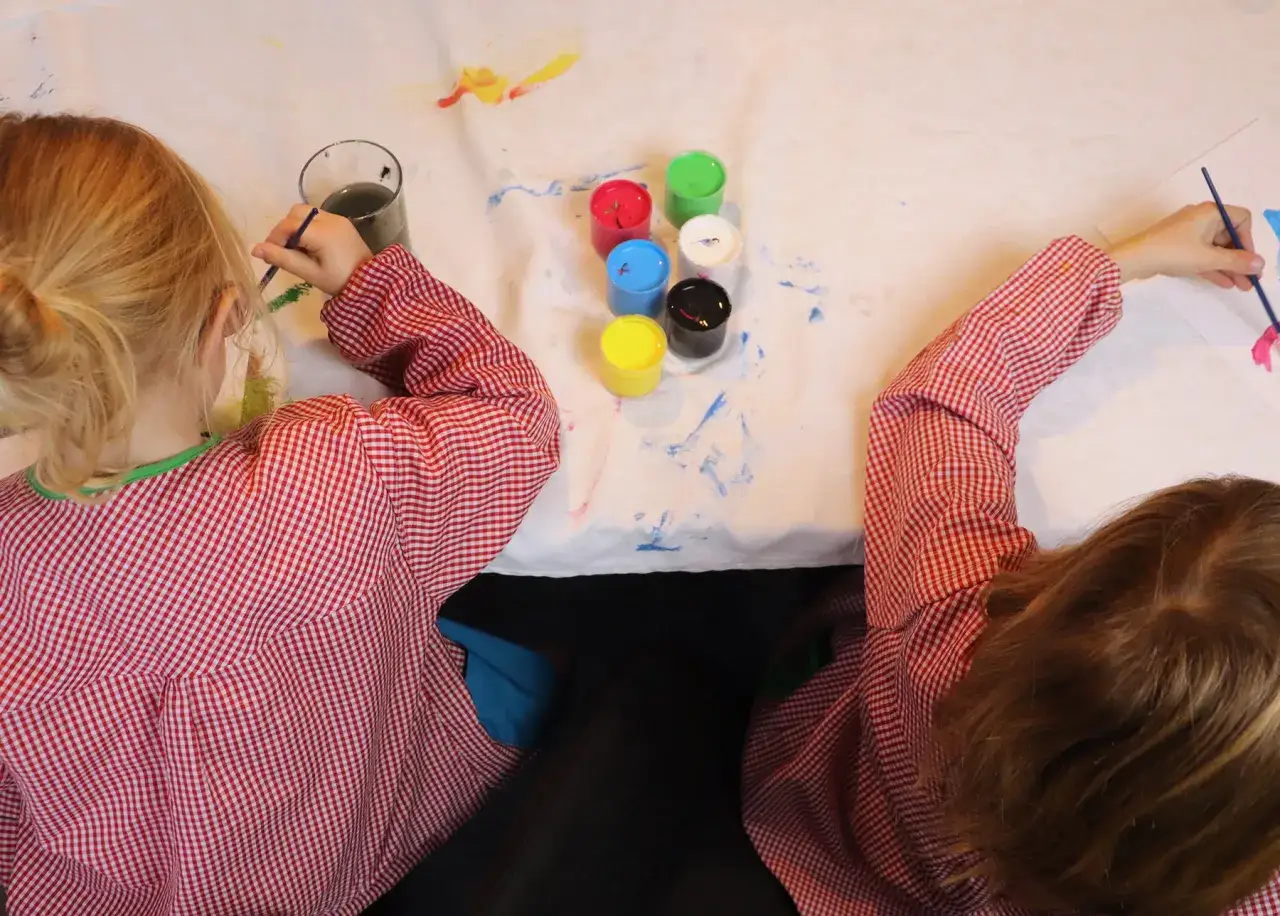 Dos niños disfrutan de pintar con niños, con pinceles y botes de pintura de colores sobre una mesa.