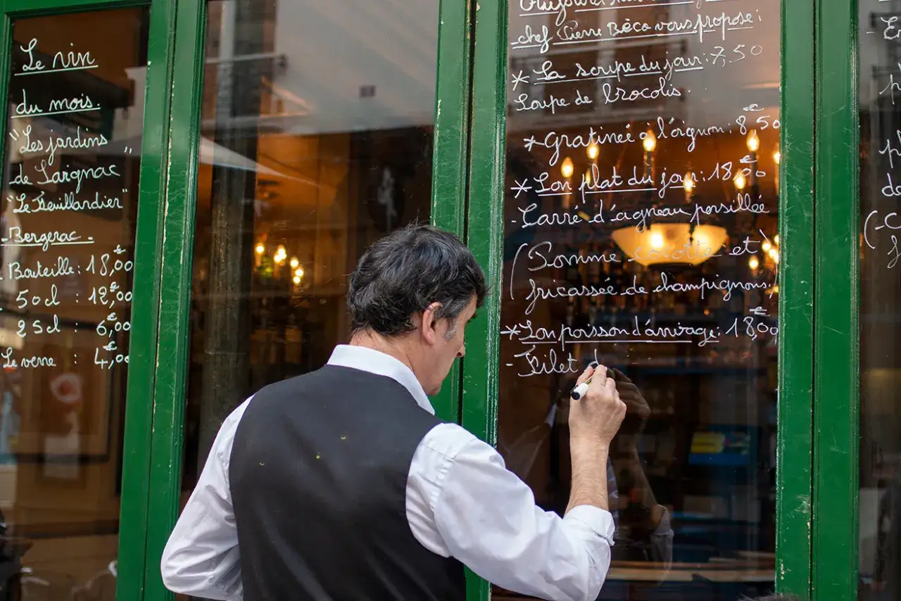 Hombre escribe frases restaurante en cristal. Men&uacute; del d&iacute;a con precios.
