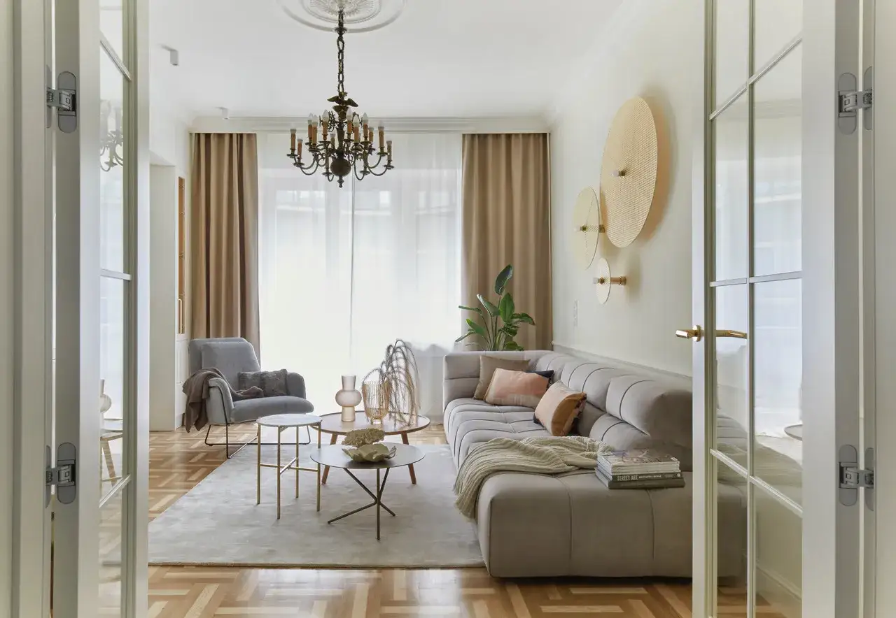 Przytulny salon w stylu francuskim: szara sofa, fotel, stoliki kawowe i ozdobne talerze na ścianie.