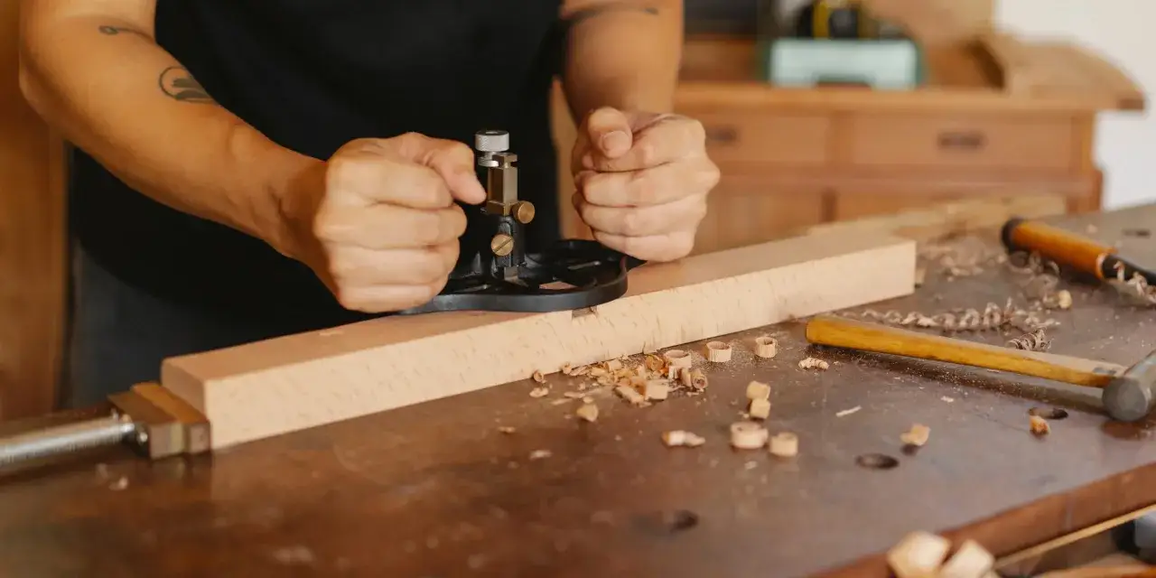 Carpintero usando una cepilladora para alisar madera, una t&eacute;cnica para lijar madera sin lija. Virutas de madera esparcidas.