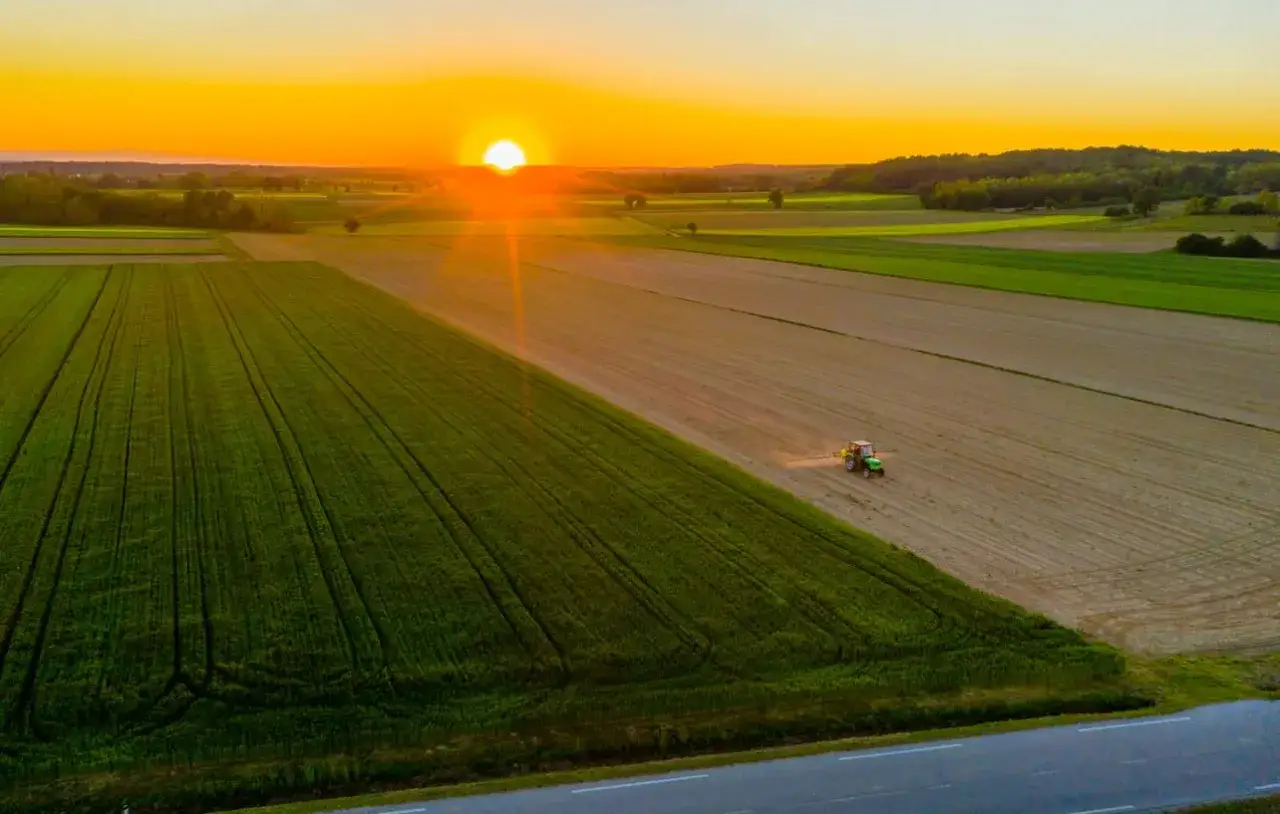 Zachód słońca nad polem, gdzie traktor przygotowuje teren pod przekształcenie działki rolnej na budowlaną.