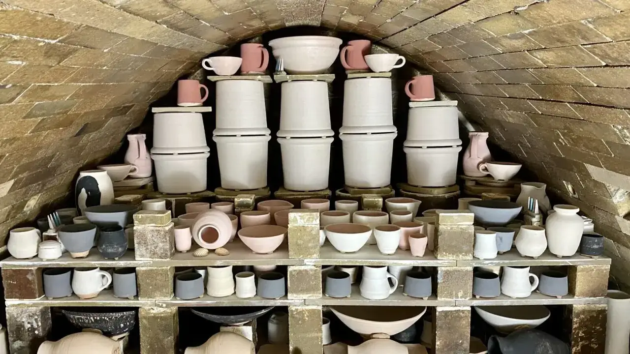 Wypalane naczynia ceramiczne, w tym misy i kubki, czekają na wypalenie. Kamionkowy materiał budowlany pieca tworzy unikalną atmosferę.
