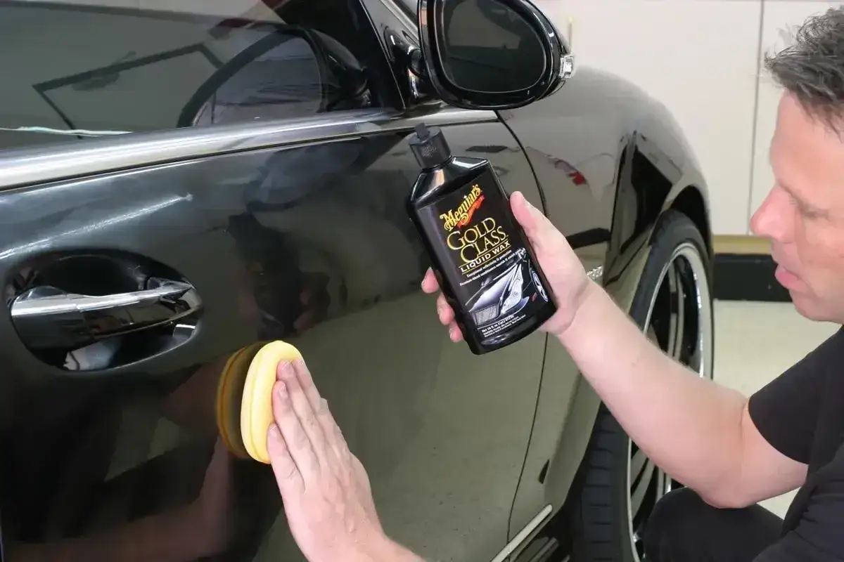 Mężczyzna nakłada wosk na czarne auto. Czy po woskowaniu płukać auto? Dowiedz się, jak uzyskać idealny połysk.