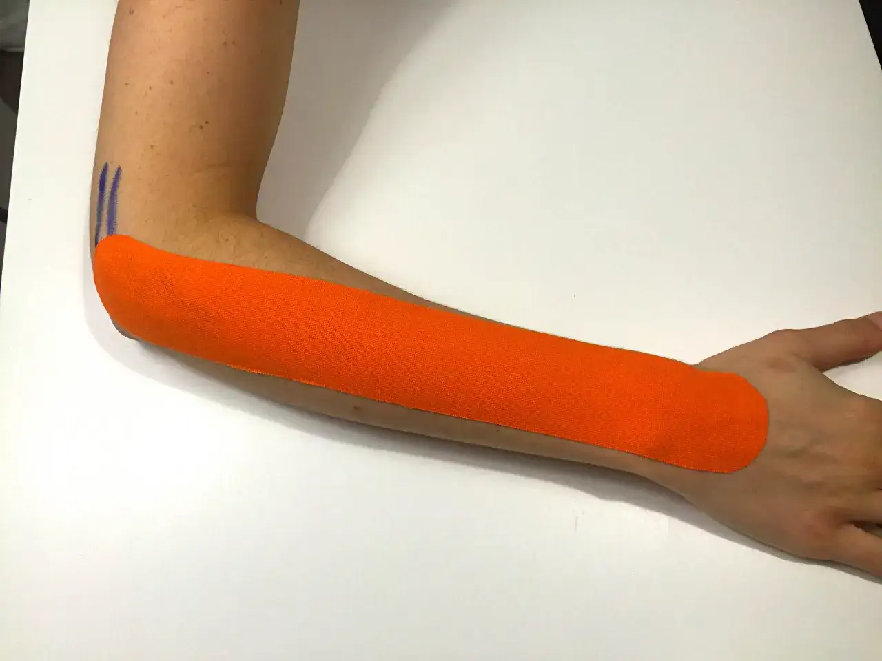Pomarańczowy plaster kinezjotaping na przedramieniu, wspierający w leczeniu łokcia tenisisty.