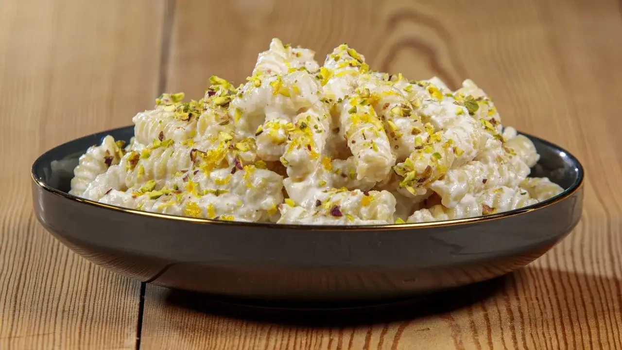 Pasta ricotta e limone cremosa, guarnita con pistacchi tritati e scorza di limone, servita in una ciotola scura su un tavolo di legno.