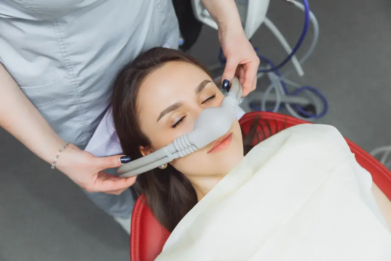 Kobieta z zamkniętymi oczami wdycha gaz rozweselający u dentysty. Znieczulenie u dentysty działa szybko, łagodząc stres.