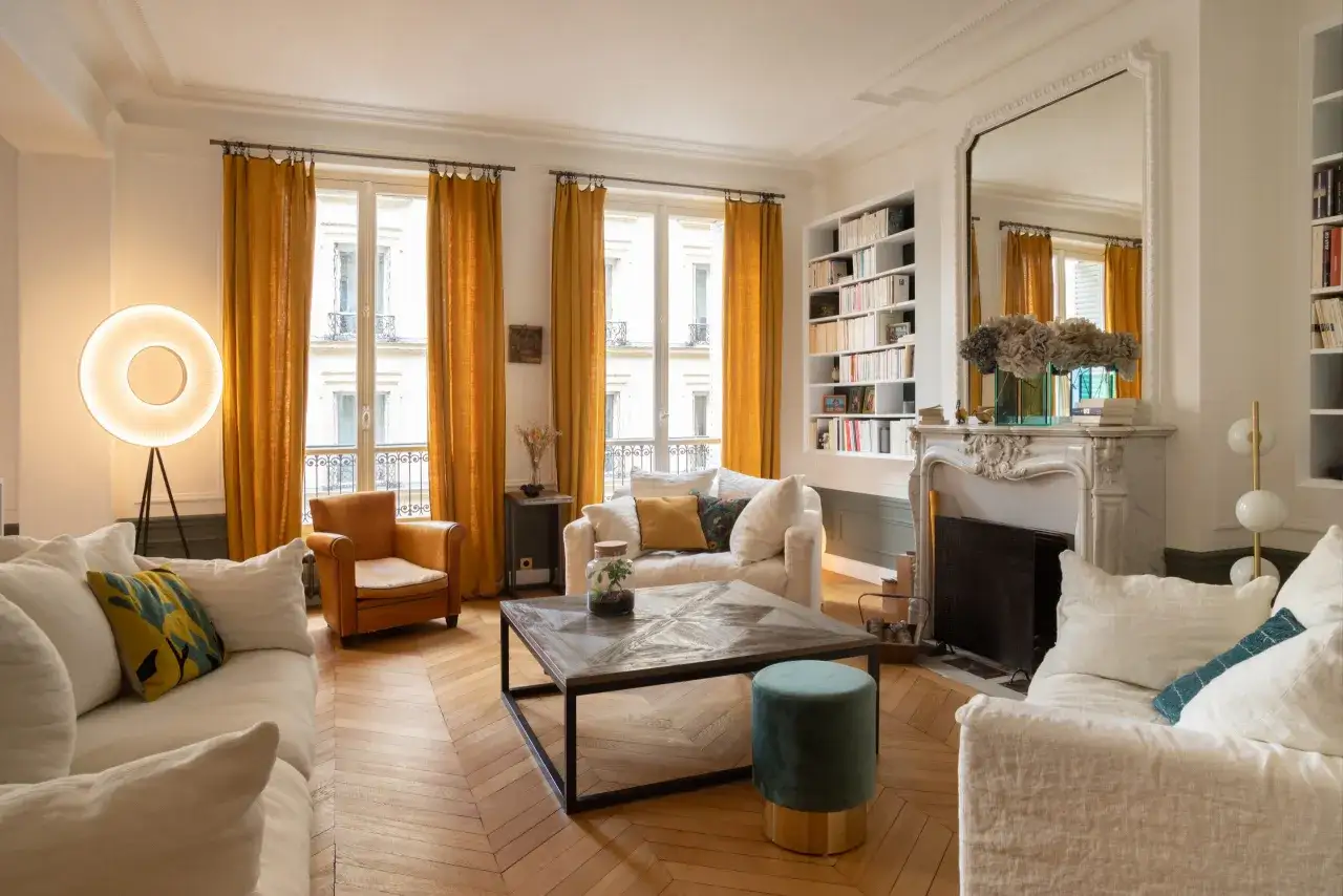 Salon lumineux avec rideaux ocre, canapés blancs et fauteuil cuir. Quelle couleur avec meuble Louis Philippe ? Le doré des rideaux et le cuir du fauteuil s'accordent bien.