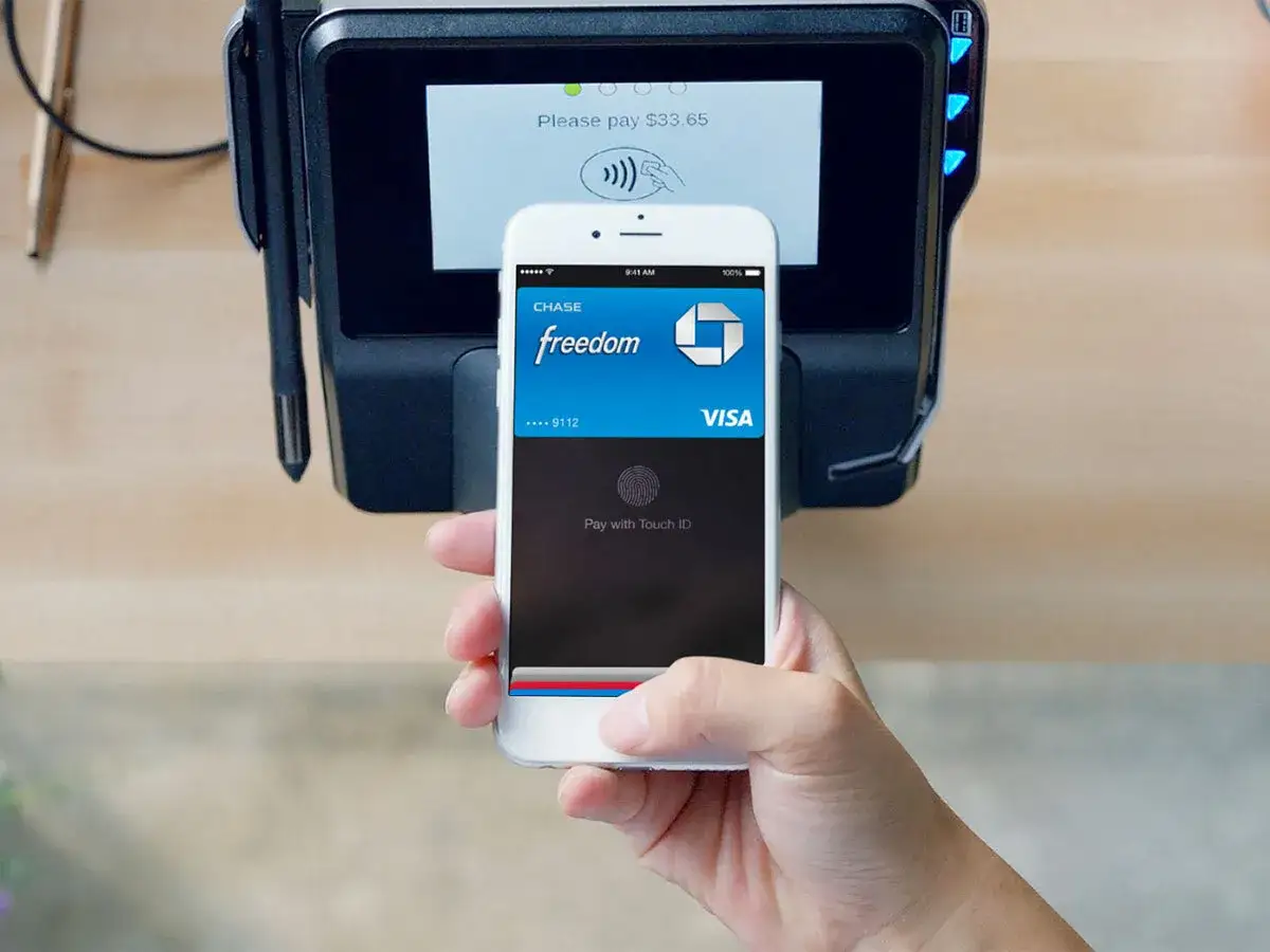 Płatność zbliżeniowa iPhone'em z użyciem NFC. Dłoń trzyma telefon, zbliżając go do terminala płatniczego.