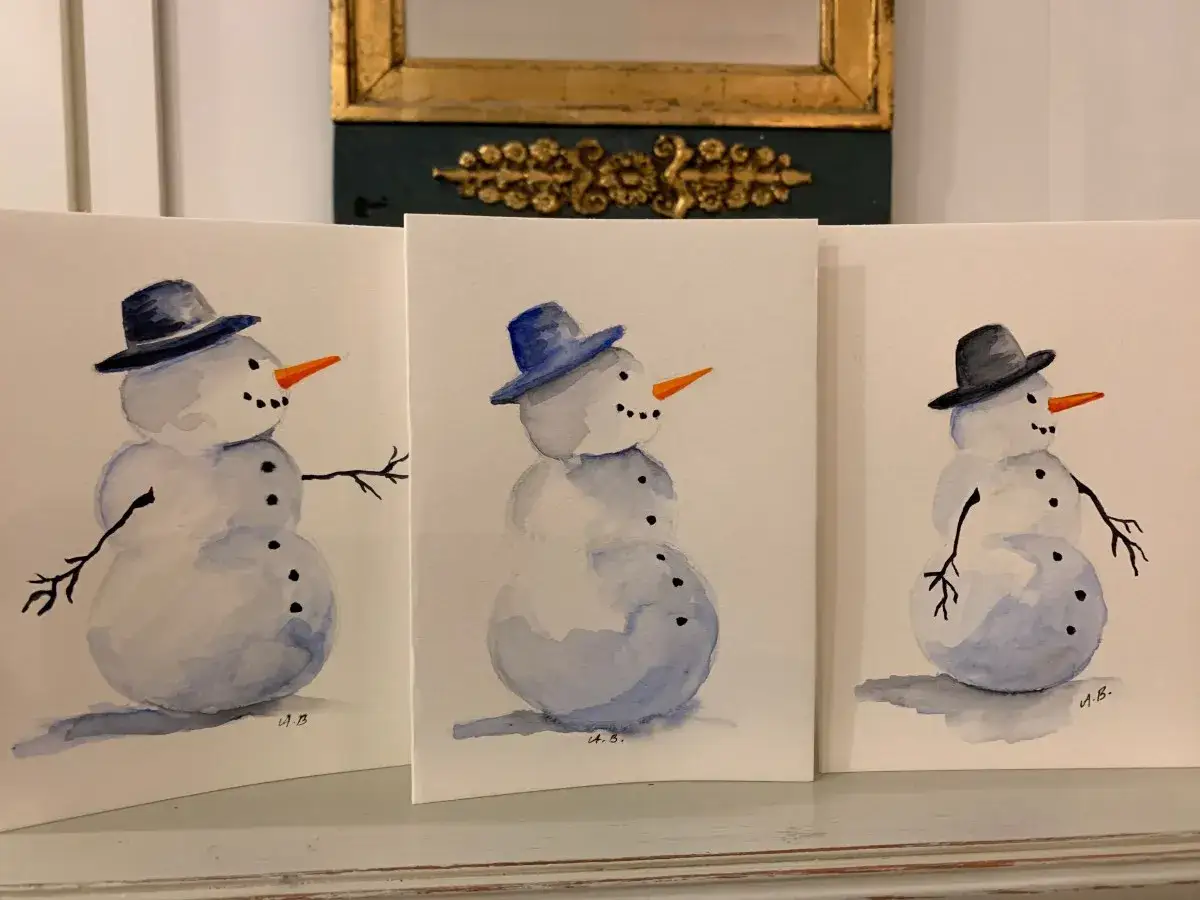 Tre akvarellmålade snögubbar med hattar och morotsnäsor, redo att skickas som julkort.