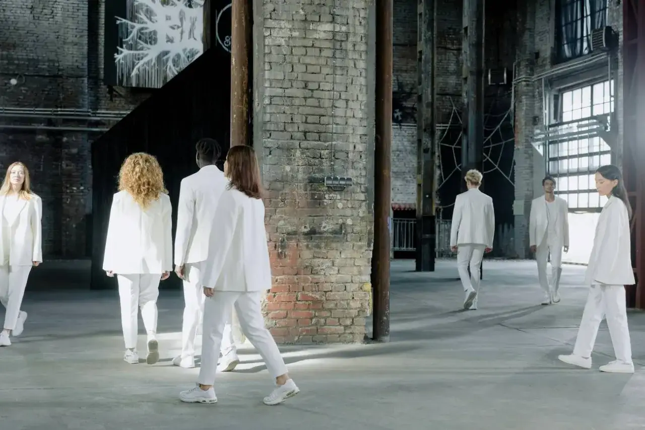 Un grupo de personas vestidas de blanco camina en un espacio industrial. Parecen bailarines, cada uno con un estilo único, como un cloud dancer color.