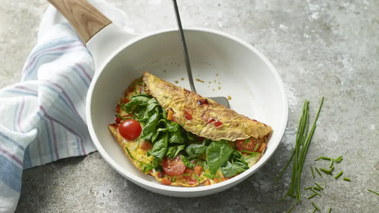 Pyszny omlet low carb z pomidorkami, szpinakiem i szczypiorkiem, gotowy do podania na śniadanie.