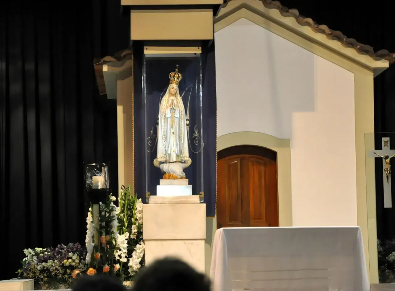 Figurka Matki Bożej Fatimskiej w ołtarzu, symbol objawienia fatimskiego, otoczona kwiatami i świecą.