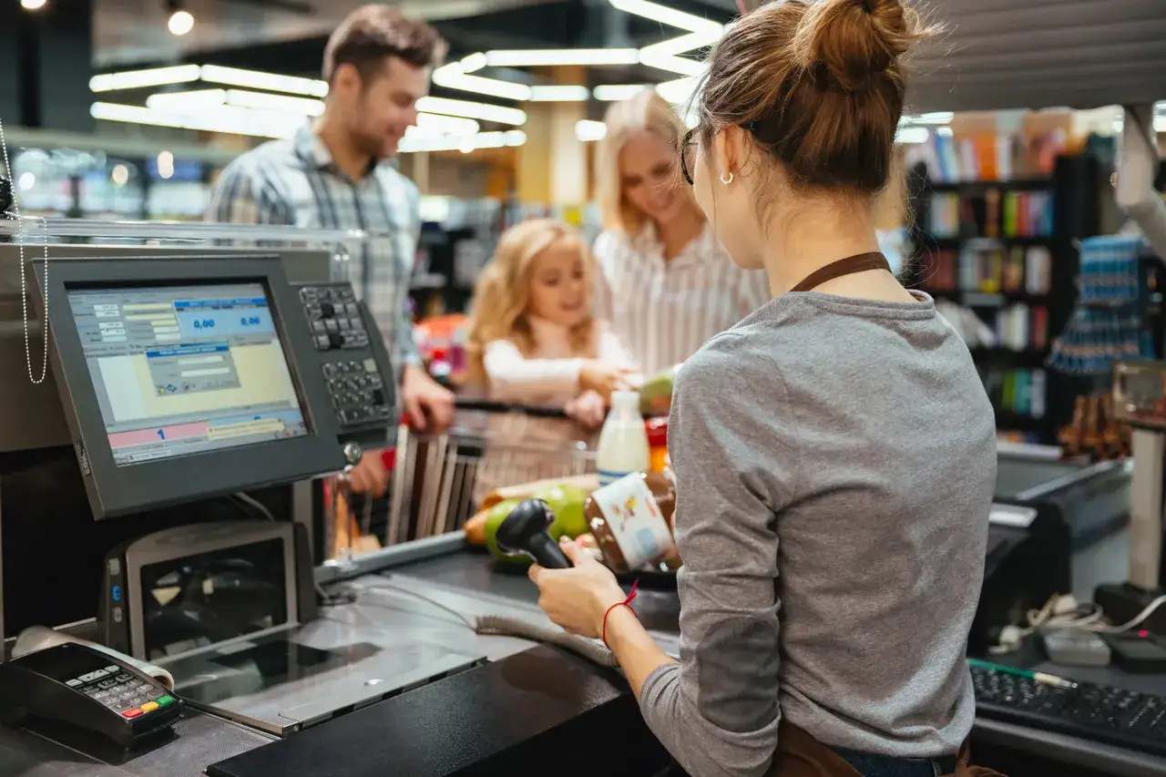 Kasjerka w sklepie spożywczym obsługuje rodzinę przy kasie. Branza retail w akcji.