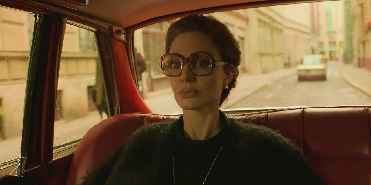 Angelina Jolie i en bil, med stora glasögon och en mörk tröja. En scen från en av hennes filmer.
