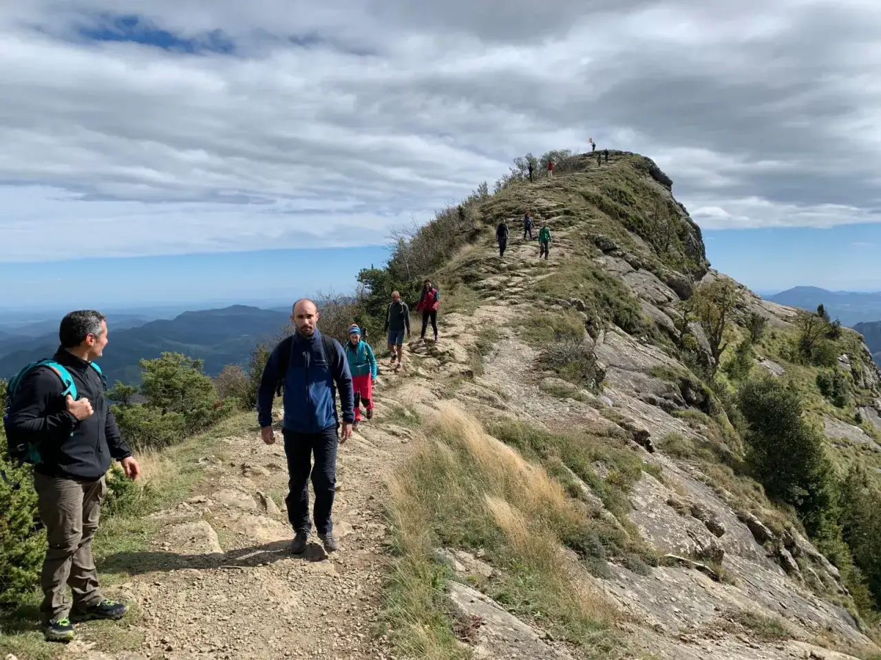 Grupo de senderistas en la **ruta Puigsacalm**, disfrutando de un paisaje monta&ntilde;oso con vistas al valle.