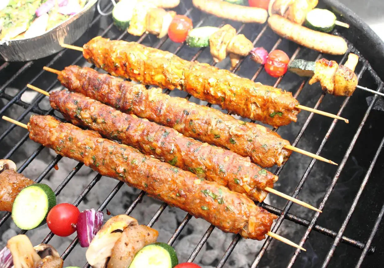 Gruzińskie szaszłyki z mięsa mielonego, pachnące ziołami, pieką się na grillu obok warzyw.
