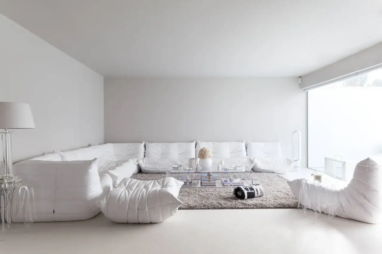 Soggiorno minimalista dominato da diversi tipi di bianco: divani modulari, pouf e arredi creano un'atmosfera eterea.