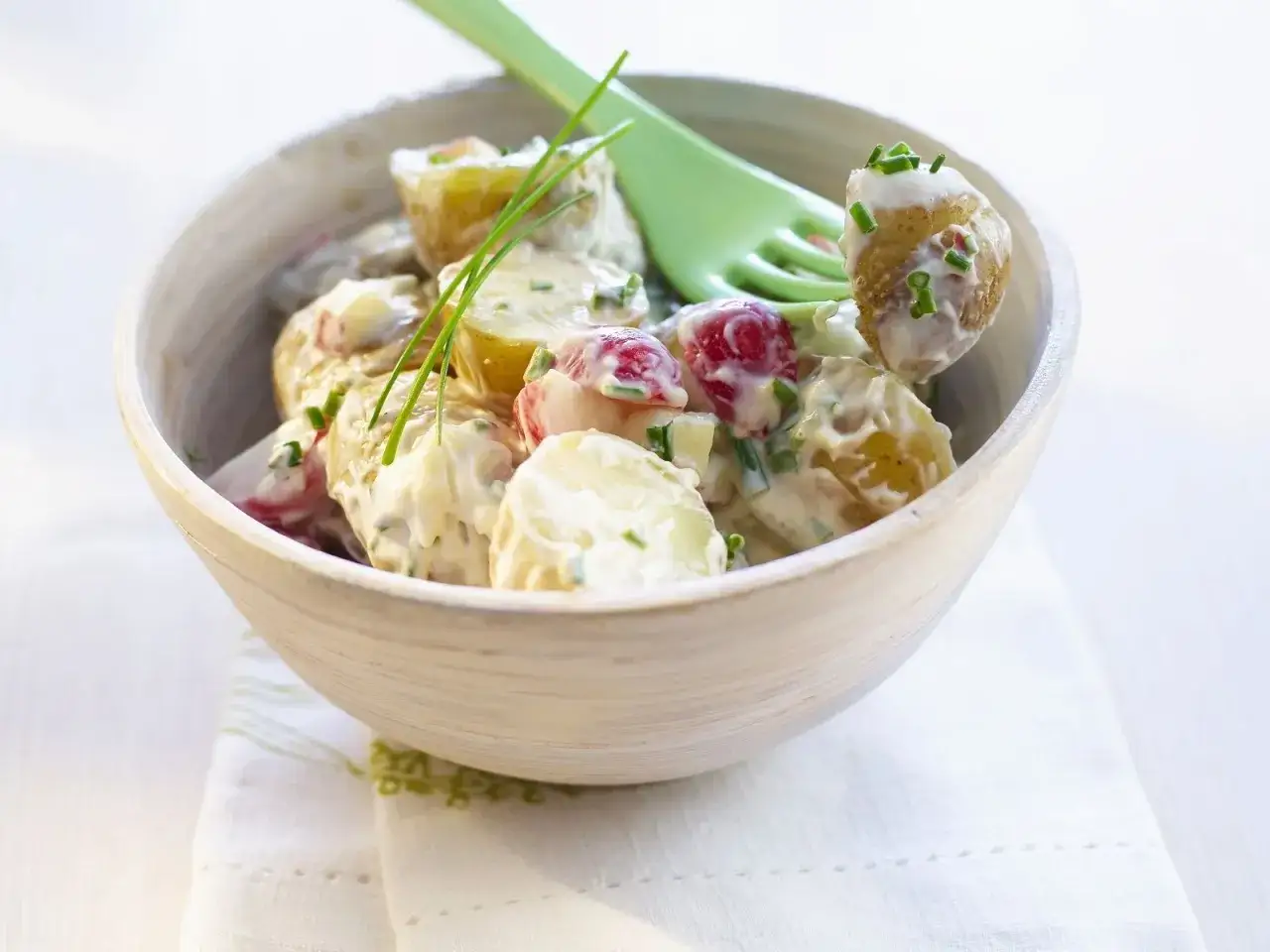Schüssel mit cremigem Kartoffelsalat mit Radieschen und Schnittlauch, garniert mit einem grünen Löffel.