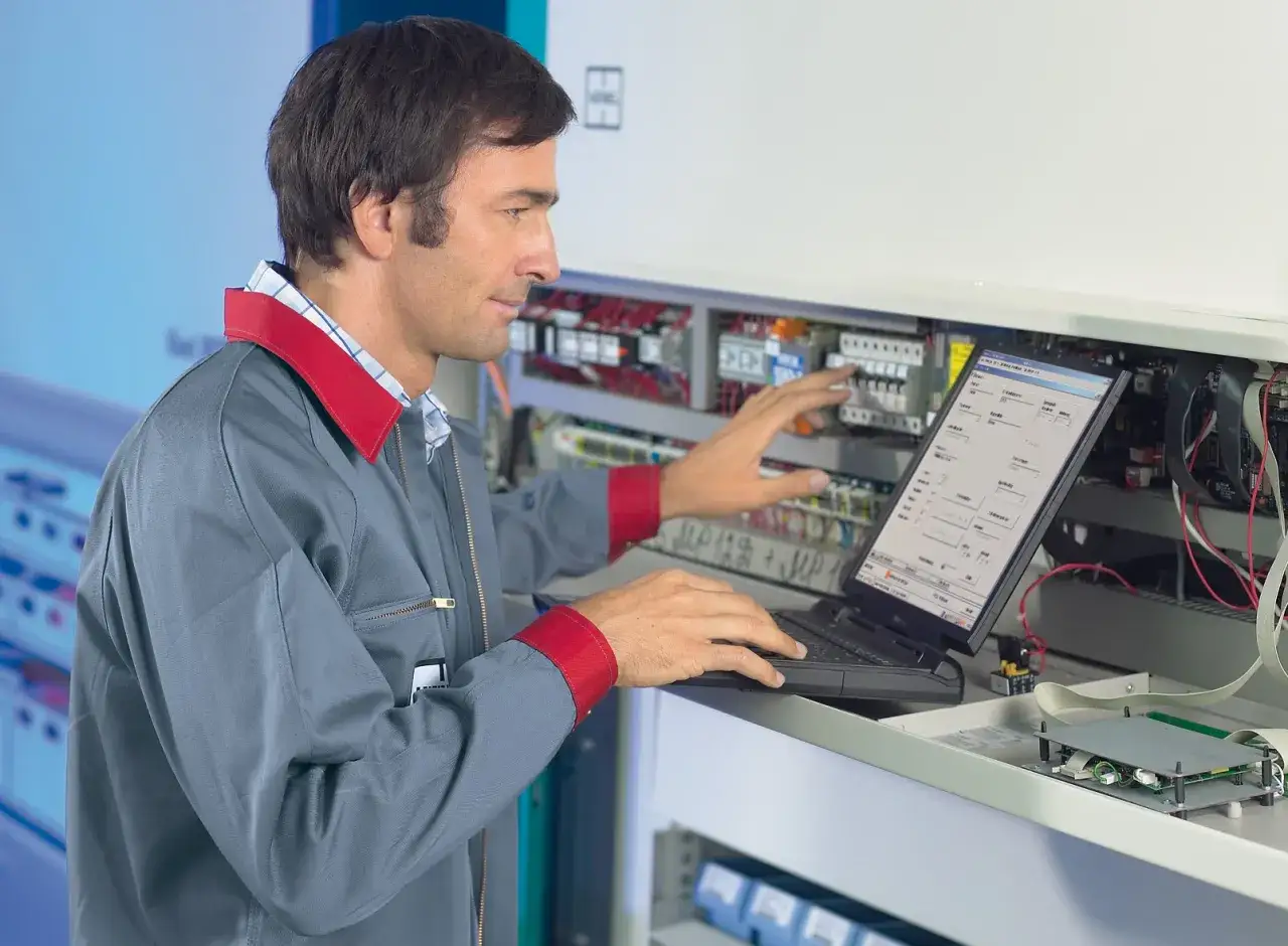 Technik z laptopem przy panelu sterowania. Dobre perspektywy dla osób z wykształceniem technicznym w automatyce i elektronice.