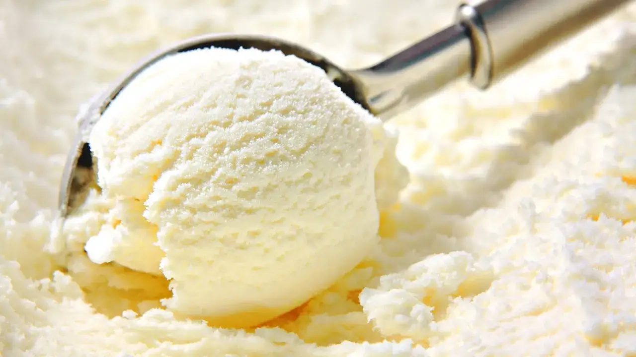 Una cuchara saca una bola cremosa de helado de vainilla, lista para ser disfrutada.