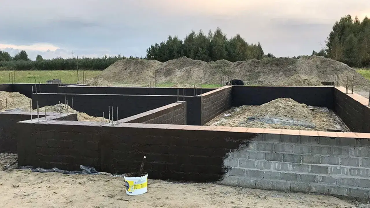 Fundament domu w budowie, ściany z bloczków betonowych pokryte ciemną masą, prawdopodobnie **bitumiczną** hydroizolacją. Wewnątrz piasek i zbrojenie.