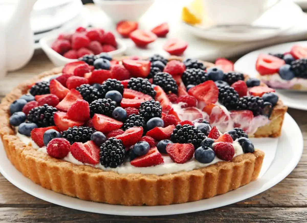 Pyszna tarta na słodko, obficie udekorowana świeżymi malinami, jeżynami, borówkami i truskawkami. Idealna na letnie popołudnie.