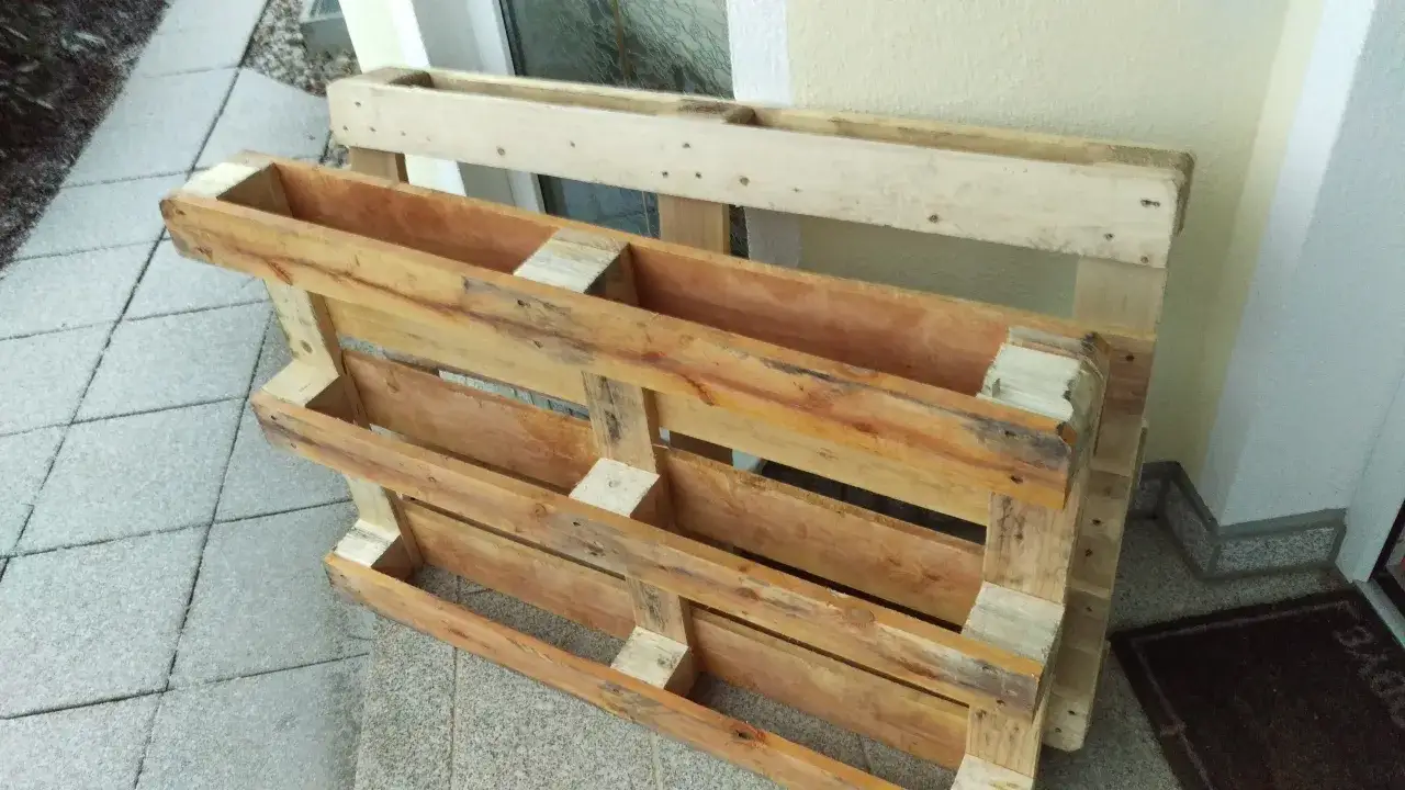 Dwa drewniane stelaże, które mogą posłużyć jako stół warsztatowy z palet, leżą na chodniku.