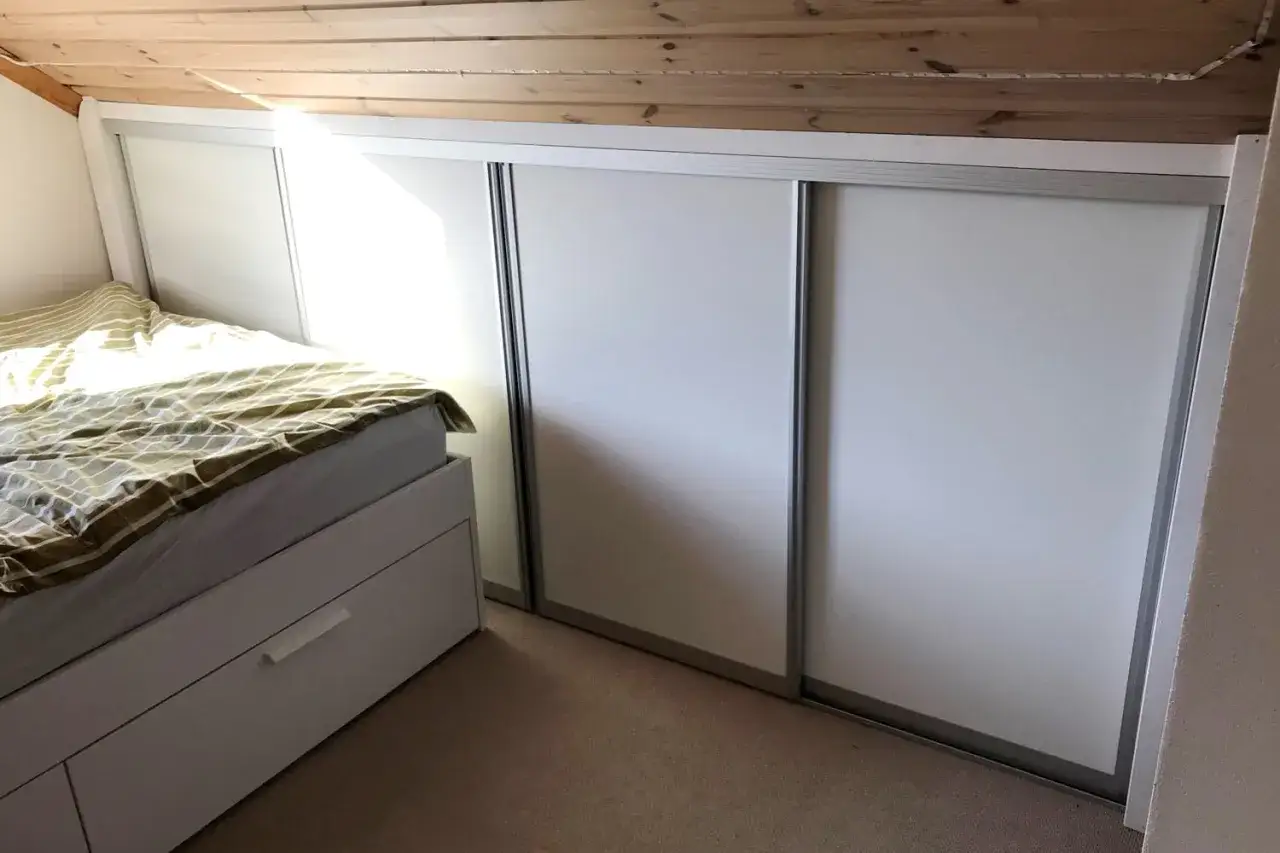 En s&auml;ng med randigt t&auml;cke bredvid en stor garderob i en kattvind.