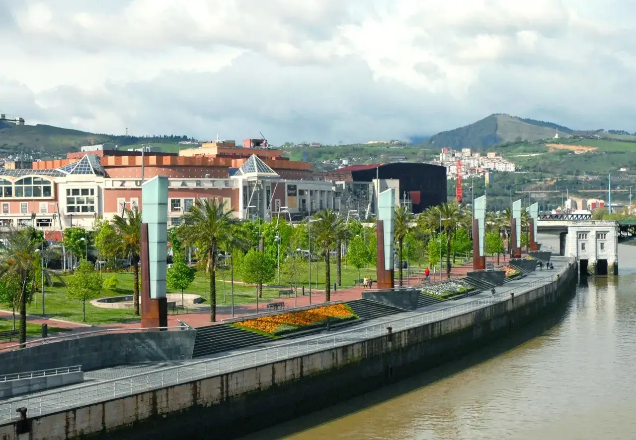 Passeggiata lungo il fiume Nervi&oacute;n, ideale per scoprire cosa vedere a Bilbao in 3 giorni: palme, aiuole fiorite e architetture moderne.